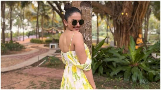 Rakul accessorised the dress minimally with aqua blue embellished slip-on sandals, rings, gold earrings, and retro-style tinted sunglasses. Lastly, she chose a pulled-back top knot, glossy nude lip shade, rouge on the cheekbones, beaming highlighter, and feathered brows for the glam picks. 