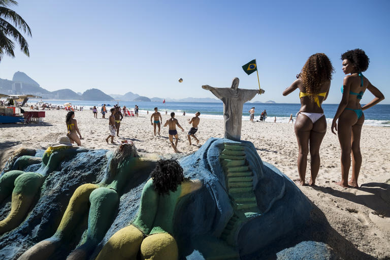 A group of friends play a game of football on Copacabana beach with a sand sculpture of “cariocas” sunbathing whilst Christ the Redeemer keeps a watchful eye, Rio de Janeiro. Christopher Pillitz/Getty Images