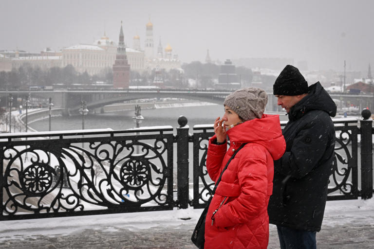 People walk on the Patriarch Bridge over the Moskva river, with the Kremlin seen in distance, during a snowfall in Moscow on November 24, 2023. Tens of thousands of Muscovites don't have heat and water in their homes.
