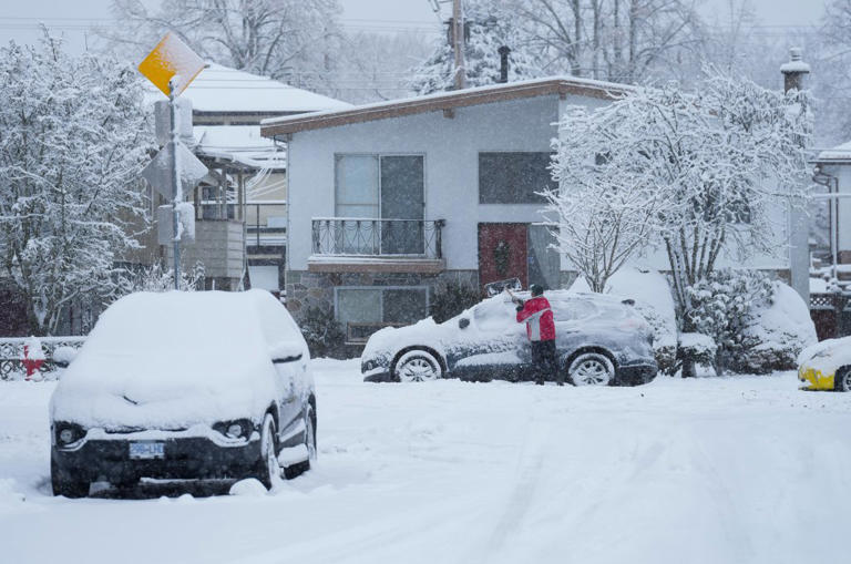 A man uses a shovel to remove snow from the roof of a vehicle as snow falls in Vancouver, on Sunday, December 18, 2022.