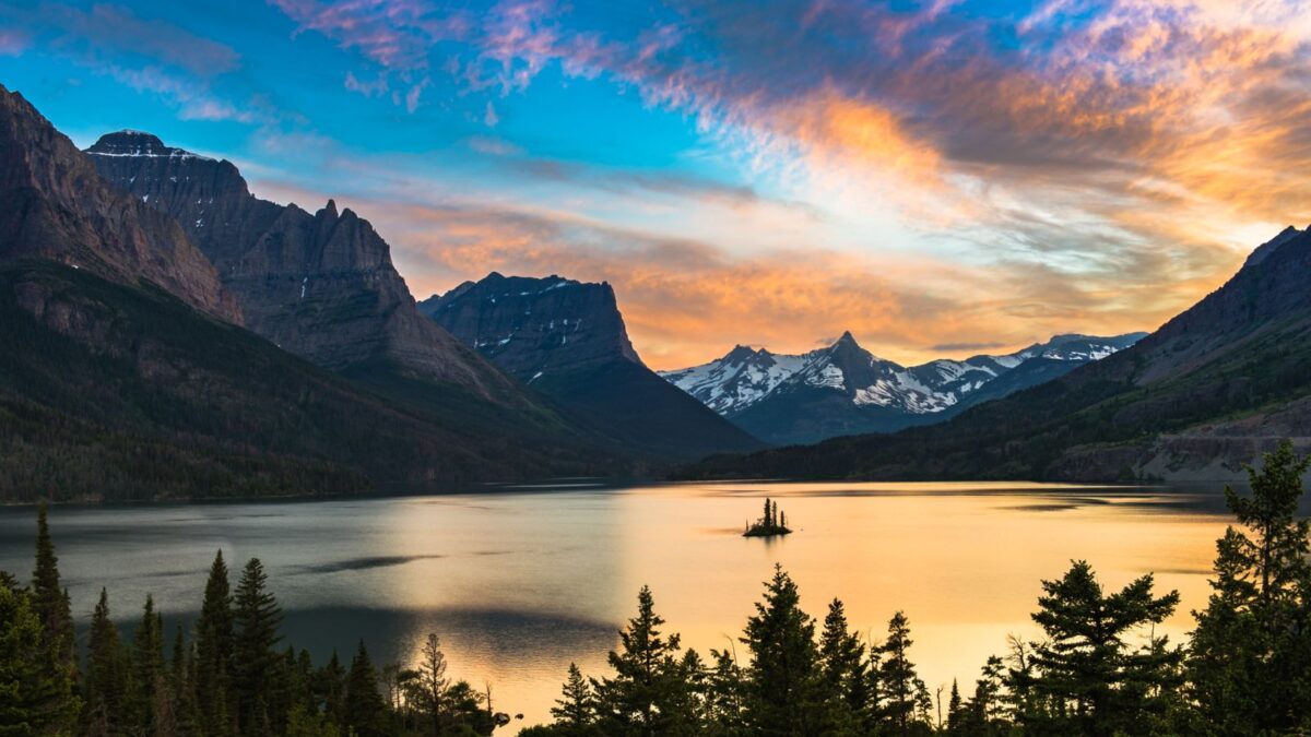 Sunset at St. Mary Lake in Glacier National Park with vibrant orange and pink clouds in the sky above tranquil waters and silhouetted mountains.