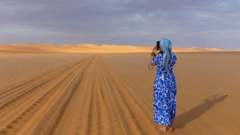 A woman in long dress and headscarf takes a photo of a Rub al Khali sand dune in Saudi Arabia - Eric Lafforgue/Art in All of Us/Corbis/Getty Images