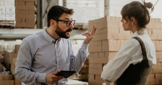 A male manager has a conflict with a female worker, while both standing in a warehouse.