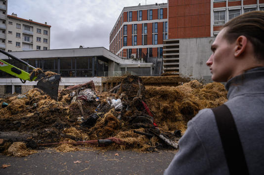 A bystander watches as farmers from the Midi-Pyrenees region of southwest France dump manure and rotting produce outside a government administrative building as they take part in a protest against taxation, declining income and difficult work conditions, in central Toulouse, Jan. 16, 2024. / Credit: ED JONES/AFP/Getty