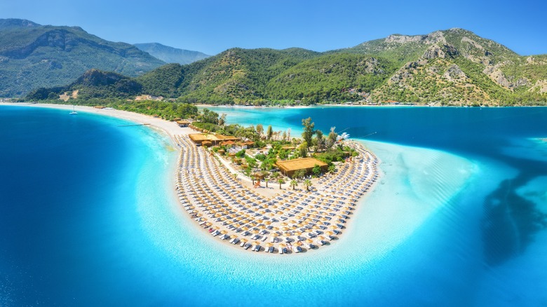 <p><span><span><span><span><span><span>Located on Turkey's southwestern coast, Ölüdeniz is a coastal gem that seamlessly combines azure waters, pristine beaches, and rugged mountainous terrain. The centerpiece of this idyllic scene is the Blue Lagoon, a stunning stretch of calm, turquoise waters framed by a curving golden shoreline and surrounded by lush greenery.</span></span></span></span></span></span></p>  <p><span><span><span><span><span><span>The contrast of the vibrant blue of the lagoon against the backdrop of the Babadağ mountain creates a mesmerizing visual spectacle. Paragliders take off from the mountain's summit, providing an aerial perspective of Ölüdeniz's beauty. The Babadağ massif, clad in pine forests, stands above over the tranquil bay, offering hiking opportunities for those seeking panoramic views.</span></span></span></span></span></span></p>  <p><span><span><span><span><span><span>The Belcekız Beach, next to the lagoon, is a crescent of sand where visitors can relax and soak in their surroundings. Ölüdeniz is not only a haven for beach lovers but also an adventure seeker's paradise with opportunities for water sports and exploration of the nearby Butterfly Valley.</span></span></span></span></span></span></p>