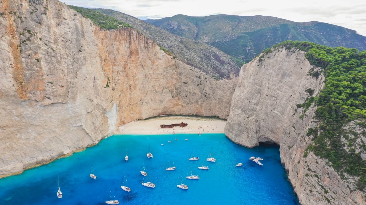 <p>This gem of the Ionian Sea is a trademark beach of Greece. <a href="https://www.navagiobeach.gr/" rel="noopener">Navagio</a> was once named “Agios Georgios,” getting its name from a shipwreck in 1980. The beach has that classic Greek beach look, with fine white sand and turquoise water. There is a tradition for whoever visits to sign themselves on the shipwreck. The beach is only accessible by water, so you should consider buying a ticket for a local ship sailing there every day.</p>