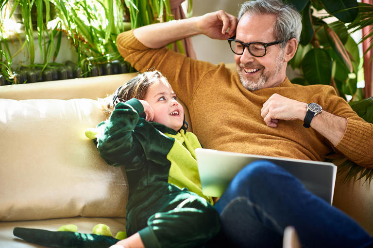 Girl in dinosaur costume smiling at mature father on sofa
