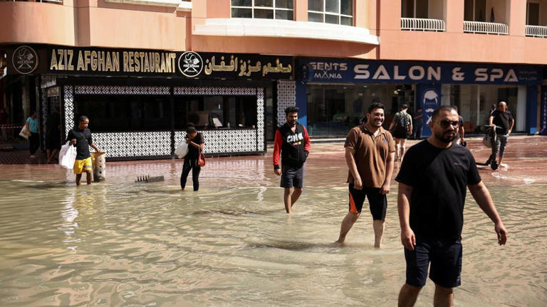 People walk through lingering floodwaters caused by heavy rains, in Dubai on April 17, 2024. - Amr Alfiky/Reuters