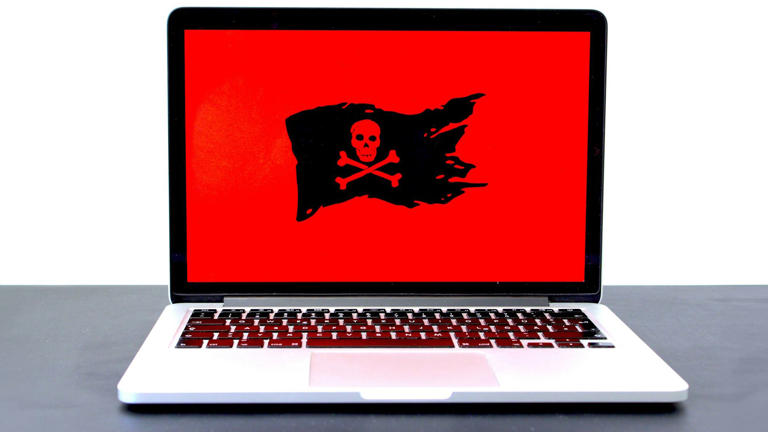 A laptop on a table displaying a large red screen with a black pirate flag symbol, indicating a potential ransomware or cyber security threat.