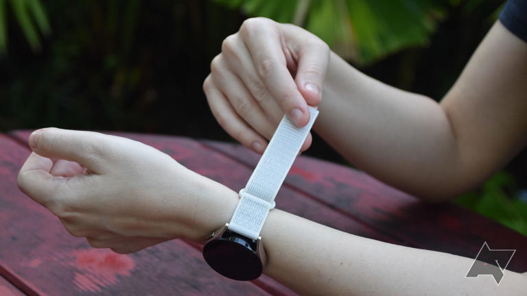 person holding white strap while wearing a galaxy watch 6 over wooden table