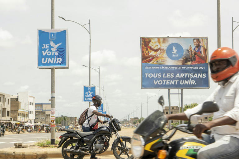 Des motocyclistes passent devant des affiches du parti au pouvoir, l'Union pour la République (UNIR), dans la capitale togolaise Lomé le 24 avril 2024