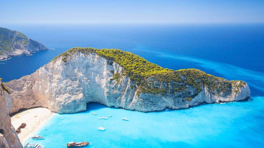 <p>Navagio Beach, more famously known as Shipwreck Beach, is one of the <a href="https://worldwildschooling.com/instagrammable-spots-on-greek-islands/">most photographed destinations in Greece</a>. Home to an old shipwreck from the 1980s, this slice of paradise sits in a beautiful secluded cove along Zakynthos’ northwest coast. </p><p>Navagio Beach, surrounded by towering cliffs, has warm white sands and crystal clear blue waters that can only be reached by boat. In May, temperatures can reach 77°F (25°C), so you’ll want to dip your toes in the refreshing water. Swimming in the waters while admiring the impressive scenery that surrounds the beach is something you won’t soon forget. Keep in mind that the beach is temporarily closed from time to time due to fear of landslides. Visit the top of the cliffs to capture the iconic photograph of Navagio, too!</p><p class="has-text-align-center has-medium-font-size">Read also: <a href="https://worldwildschooling.com/must-visit-beaches-on-the-greek-islands/">Must-Visit Beaches in Greece</a></p>
