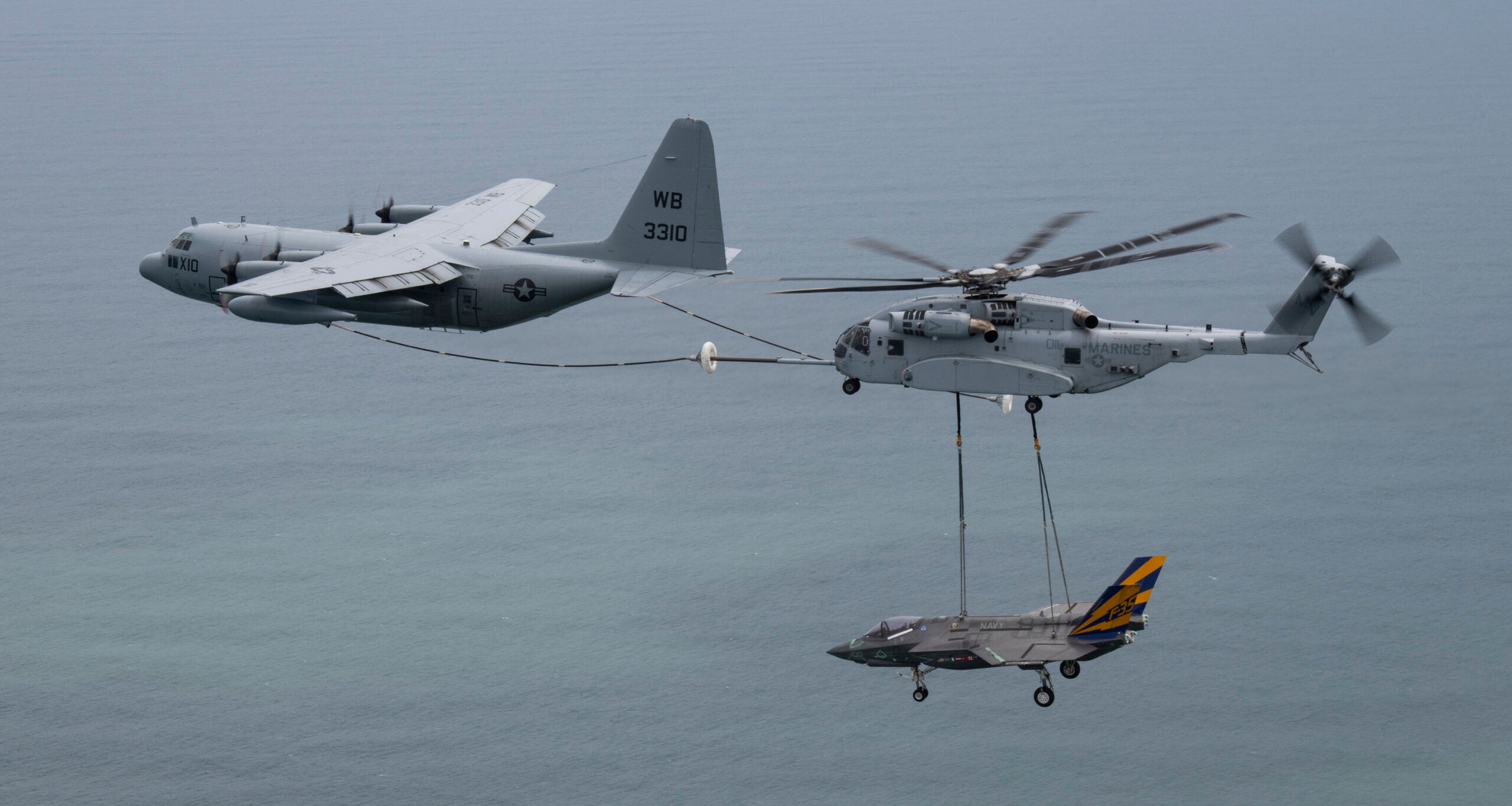 check out this navy tanker that's refueling a marine helicopter that's carrying a navy fighter