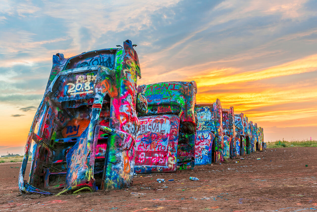 Located just west of Amarillo, Cadillac Ranch is a unique art installation featuring ten Cadillacs buried nose-down in the ground. Visitors are encouraged to bring spray paint and leave their mark on this iconic roadside attraction.]]>