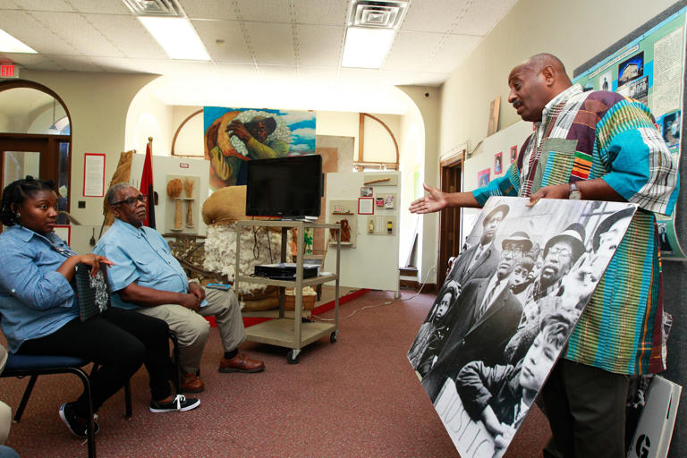 Executive director of the Wisconsin Black Historical Society Clayborn Benson holds a photo of civil rights attorney Lloyd Barbee as he talks about the Milwaukee fair housing marches to visitors from Atlanta on July 28, 2017, at the Wisconsin Black Historical Society and Museum.