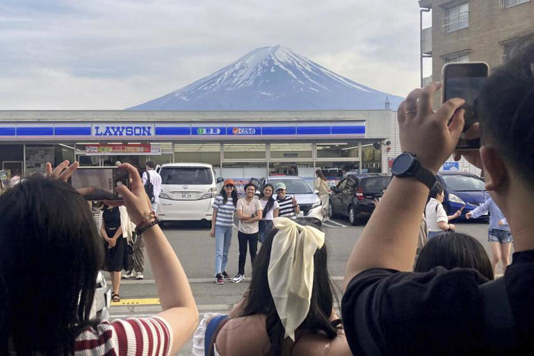 Visitors take photos of Mt. Fuji in front of a convenience store in the town of Fujikawaguchiko, Japan, on Sunday. The town has begun to set up a huge black screen on a stretch of sidewalk to block the view of the mountain. ((Kyodo News / Associated Press))