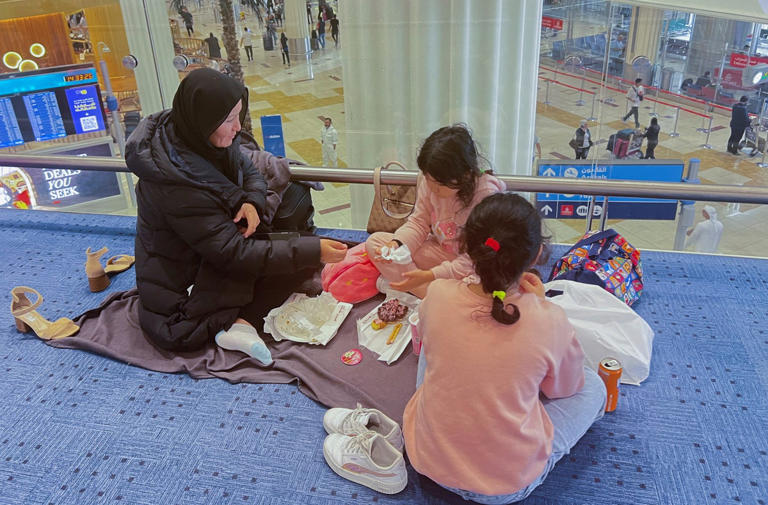 Woman and her daughters eat as they wait for their flight after a rainstorm hit Dubai, causing delays at Dubai International Airport