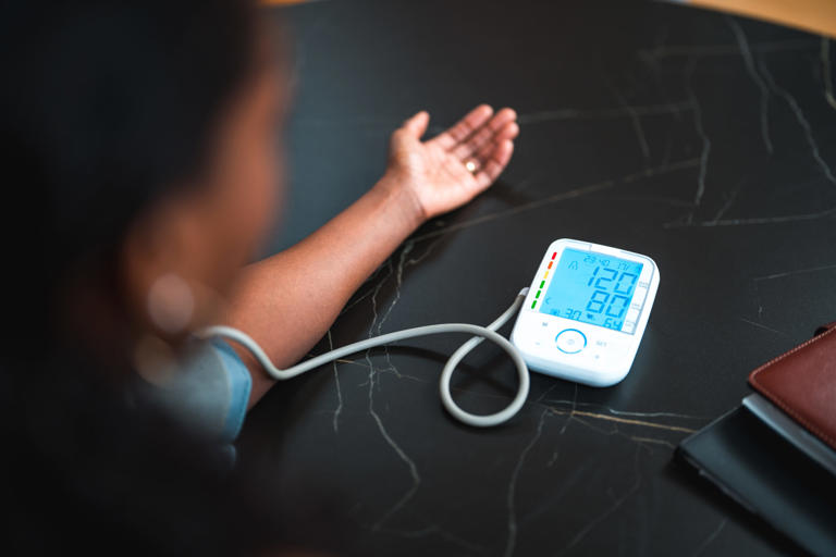 Mid adult black female using a medical device in a domestic dining room. Measuring blood pressure at home.