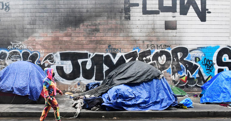 A woman walks past tents for the homeless lining a street in Los Angeles, Calif. on Feb. 1, 2021.