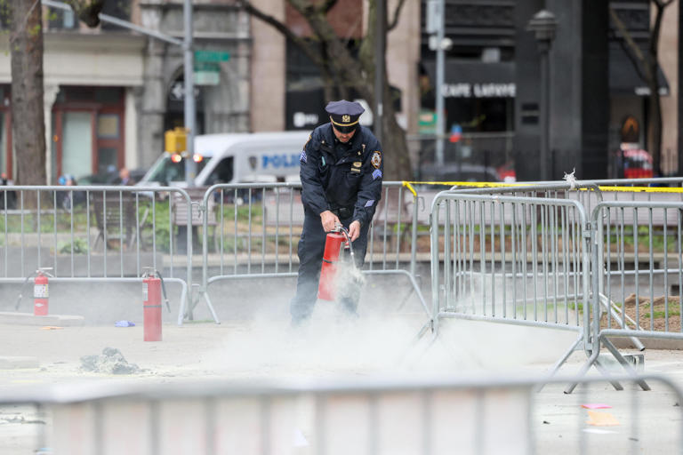 A police officer uses a fire extinguisher as emergency personnel respond to a fire outside the courthouse where former President Donald Trump's 