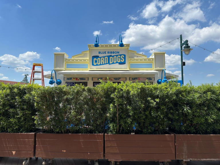 Signs have been installed on the Blue Ribbon Corn Dogs kiosk at Disney’s BoardWalk. Blue Ribbon Corn Dogs Sign The kiosk is still behind rolling planters but we can see the new signs over the shrubs. “Blue Ribbon Corn Dogs” is on the white rectangle on the front of the kiosk, above the windows. “Blue ... Read more