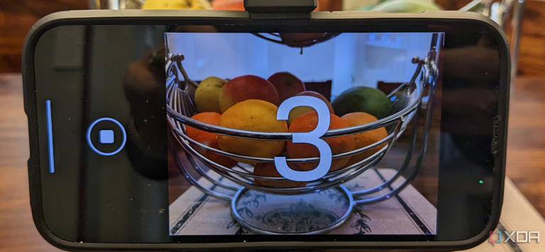 An iPhone taking a photo of a bowl of fruit with a countdown timer showing 3 seconds.