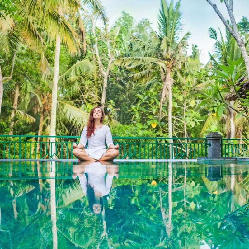 Woman meditation at gorgeous pool side of luxury tropical villa