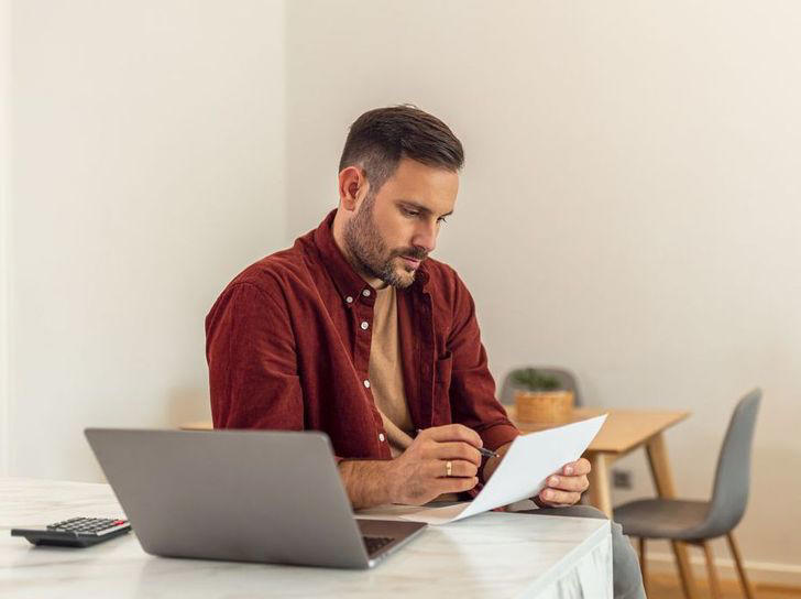 adult male entrepreneur examining a tax form while sitting in front of a laptop