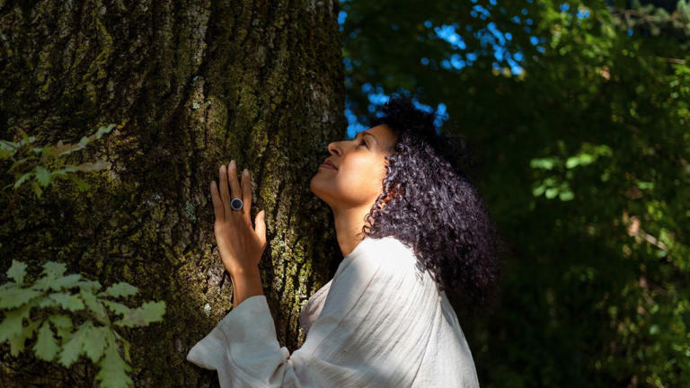 woman calm while connecting with nature by touching a large tree