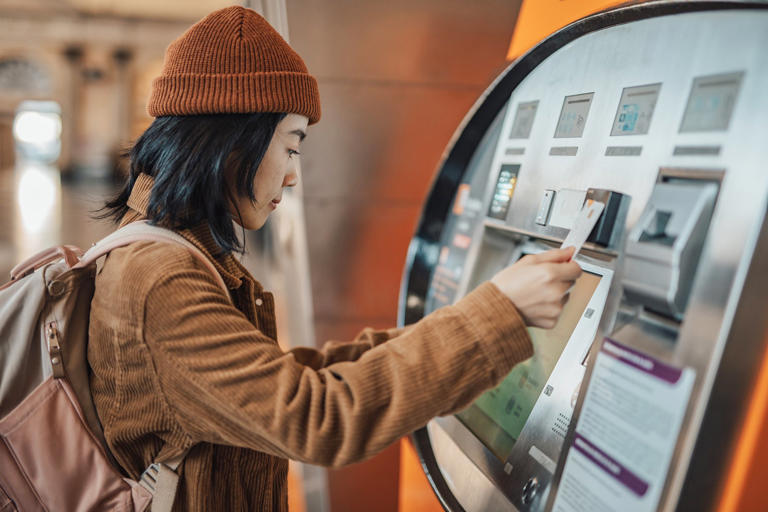 A beautiful young Chinese woman uses an ATM at a metro station in Barcelona, withdraws money to go shopping