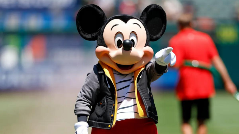 A mouse mascot wearing a black jacket, white and black striped shirt and red pants points to the right. Getty Images