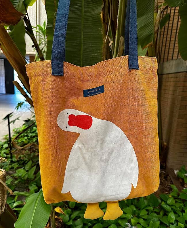 Tote bag with a cute design of a leaning white duck with an orange beak and blue label reading