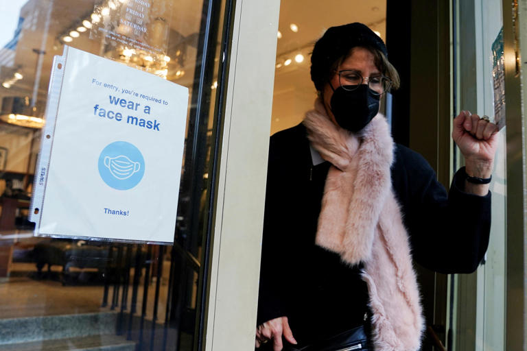 A person wearing a face mask is pictured in 2022 walking out of a store past a "Wear a face mask" sign in New York City.