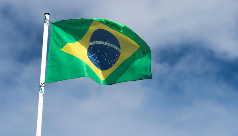 Flag of Brazil with sky and clouds in the background