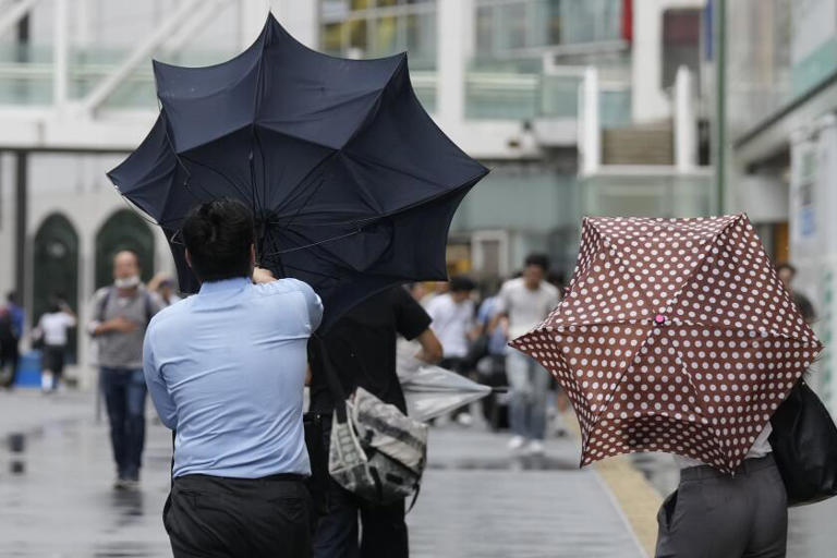 A man in Tokyo struggles with his umbrella as wind begins from Typhoon Ampil on Friday. Flights and rail travel were halted as the storm approached. ((Hiro Komae / Associated Press))