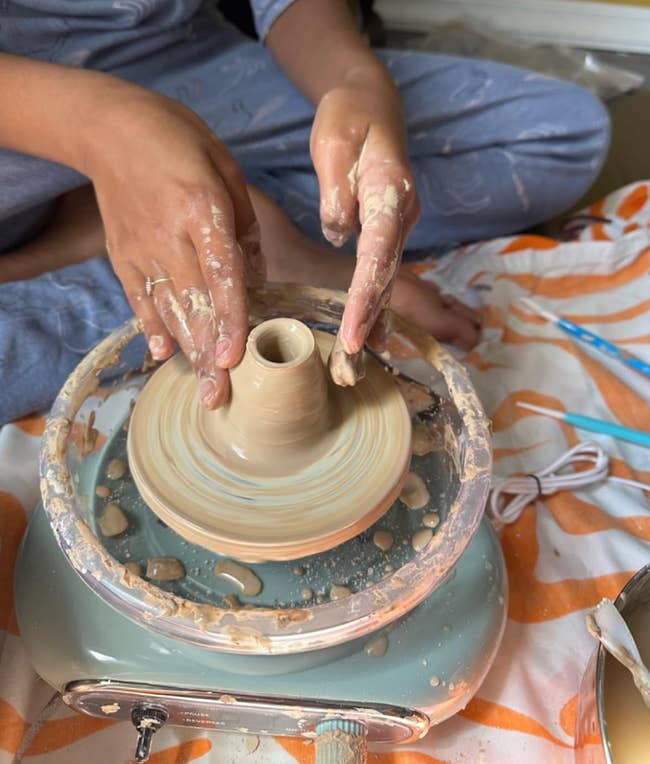 Person shaping clay on a pottery wheel, their hands covered in clay, indicating an activity in pottery making