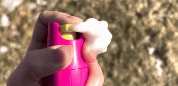 A hand spraying foam from a pink bottle