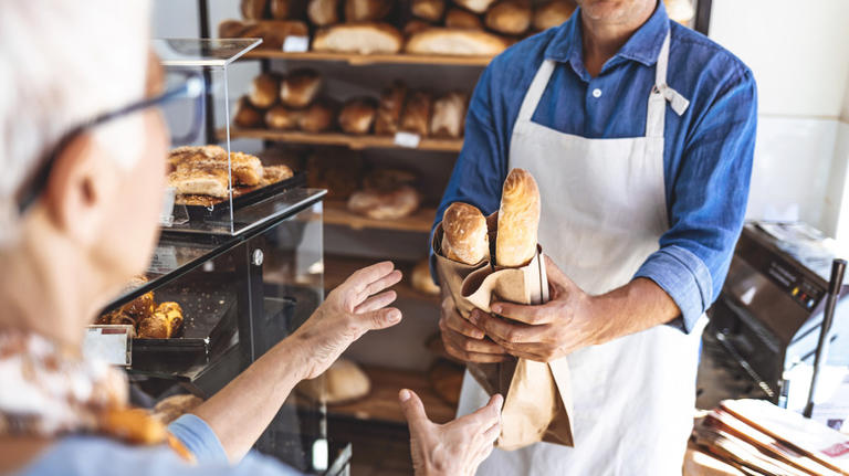 senior woman reaching for fresh bread from clerk