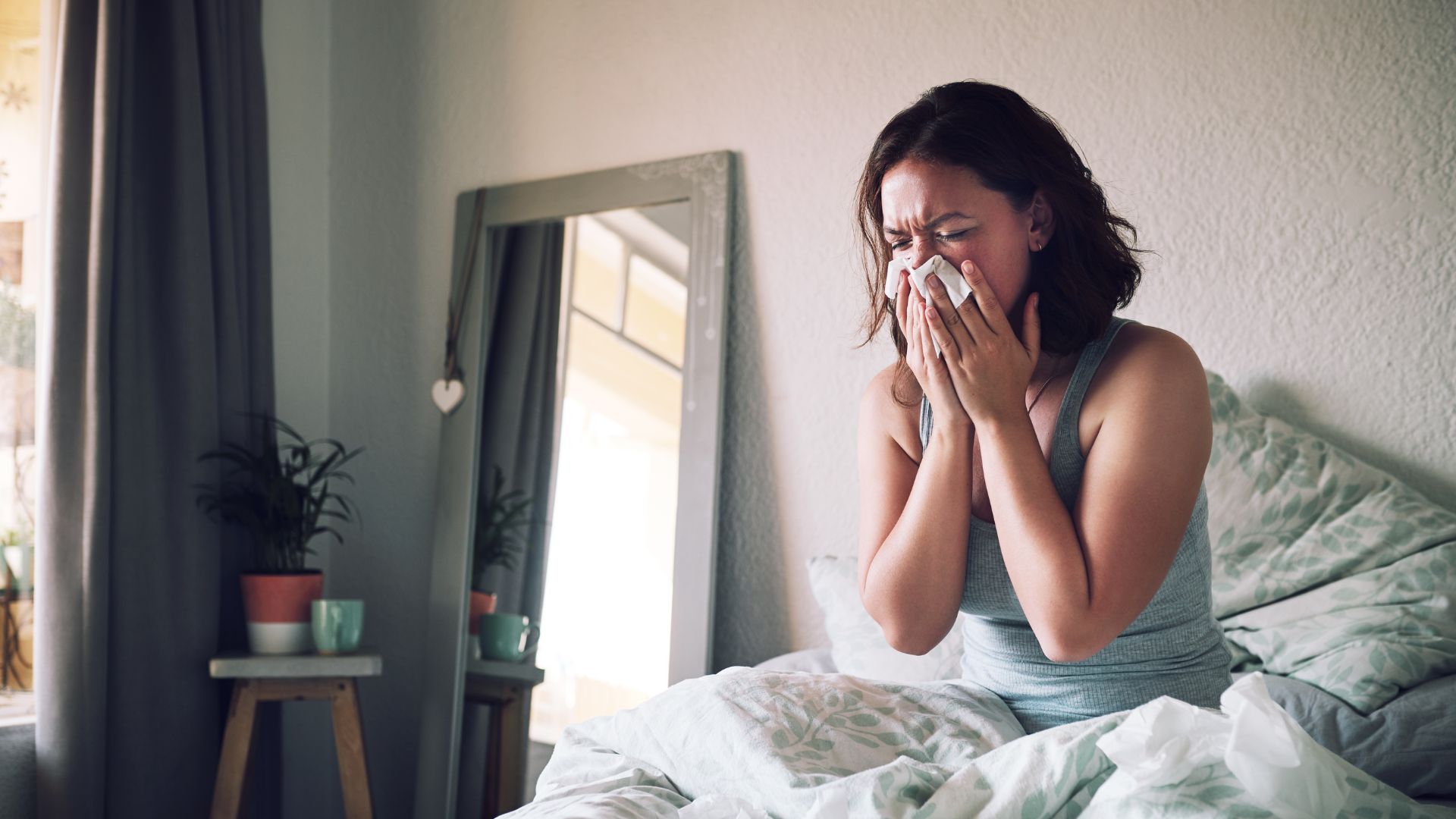 Woman blowing her nose in bed because of allergens from mattress stains