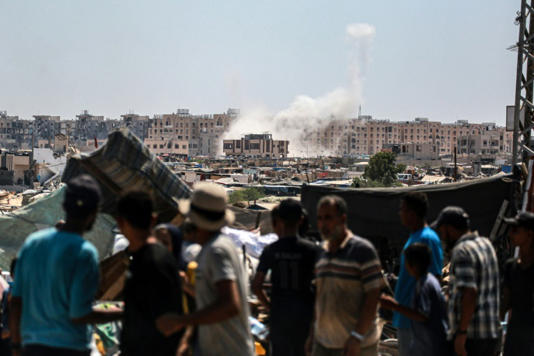 Palestinians watch from a makeshift displacement camp as Israeli shelling hits Khan Yunis in the southern Gaza Strip