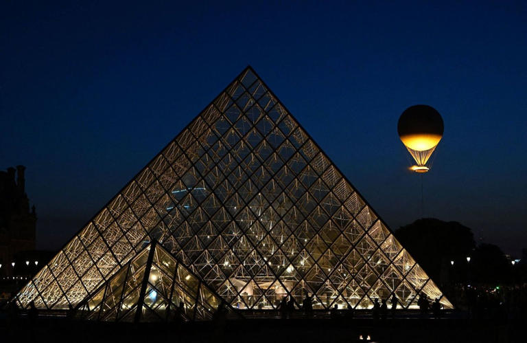 La flamme olympique flotte au dessus du jardin Tuileries et du Musée du Louvre, le 28 juillet 2024.