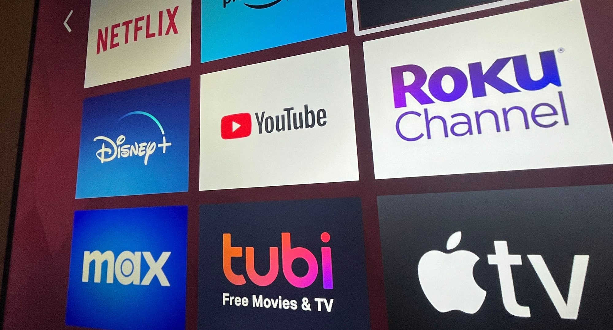 Multiple streaming services appear on a Roku TV, including Netflix, Hulu, Prime, Disney, Max, Tubi, YouTube, and Apple TV