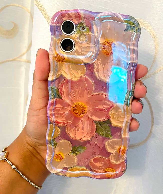 Hand holding a phone case with a floral design and clear edges, featuring large flowers in pink and white tones