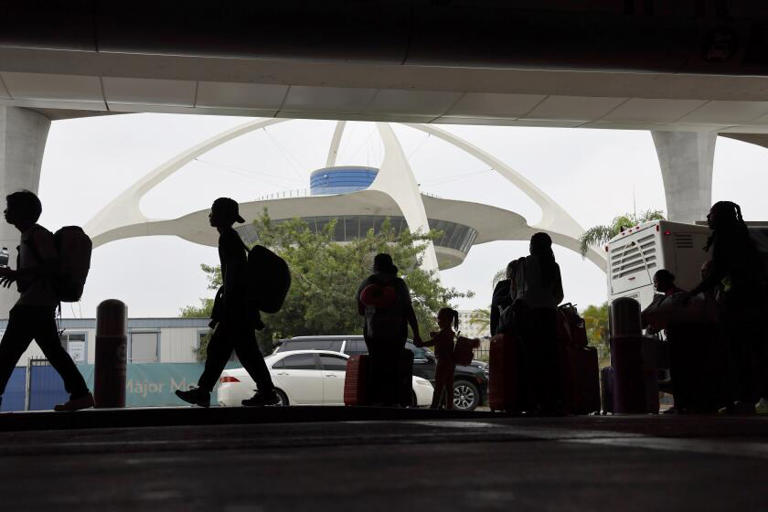 Travelers are silhouetted by the Theme Building as they arrive and find transportation while kicking off Labor Day weekend travel at Los Angeles International Airport on Thursday. ((Allen J. Schaben / Los Angeles Times))