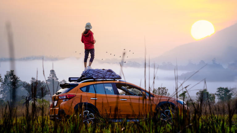 Road-tripper standing on car watching sunrise