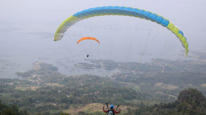 WISATA WONOGIRI - Anggota komunitas Paralayang Solo Raya terbang dari Puncak Joglo, Desa Sendang, Kecamatan Wonogiri, Jawa Tengah, Minggu (10/6/2018). Wisatawan bisa menikmati panorama keindahan alam seperti Waduk Gajah Mungkur dari udara dengan cara terbang tandem bersama instruktur paralayang bersertifikat. (KOMPAS.com/GARRY ANDREW LOTULUNG)