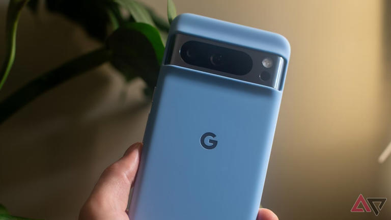 The Pixel 8 Pro in its blue Google case, held in a hand