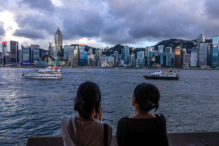 Pedestrians look out across Victoria Harbour towards the Hong Kong Island skyline in the Tsim Sha Tsui district of Hong Kong, China, on Sunday, June 23, 2024. Four years after Hong Kong began a sweeping crackdown against political dissent, the city is struggling to meet one of its own benchmarks in reassuring foreign investors that it remains a predictable place to do business.