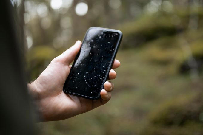 Hand holding wet smart phone in forest