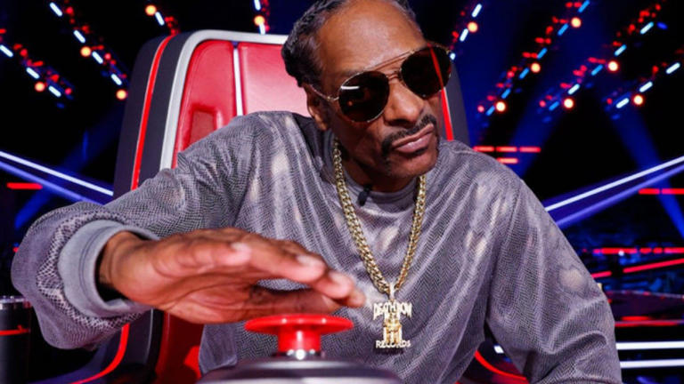 Snoop Dogg sits in his Big Red Chair on The Voice Season 26 with his hand hovering over his button.